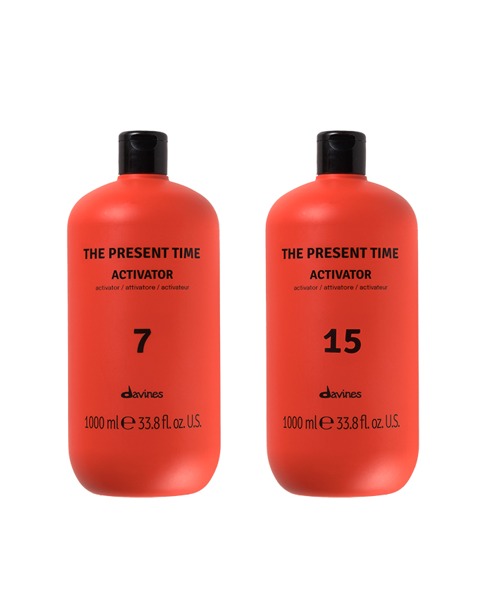 Zwei rote Flaschen des Davines 'The Present Time' Activators für demi-permanente Haarfarbe nebeneinander arrangiert. Die Verpackung ist modern und auffällig, mit minimalistischer Beschriftung. Die Produkte stehen auf einem neutralen Hintergrund, das Bild vermittelt einen hochwertigen, professionellen Eindruck – ideal für salonfähige Farbservices im Frühling 2025