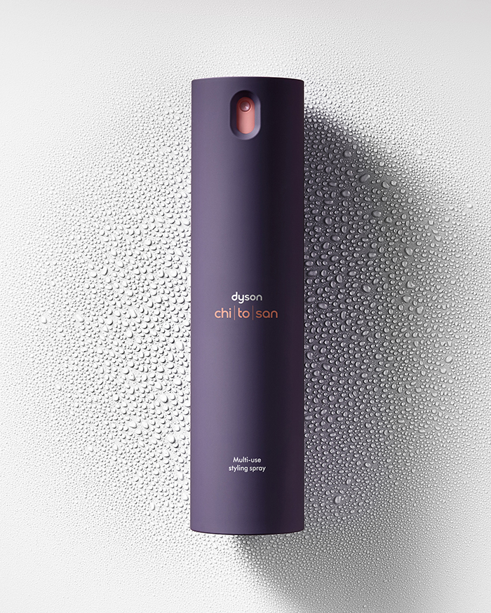 Produktfotografie eines lila Dyson multi use styling sprays auf weissem Hintergrund mit Wassertropfen für die Haarpflege an tag zwei