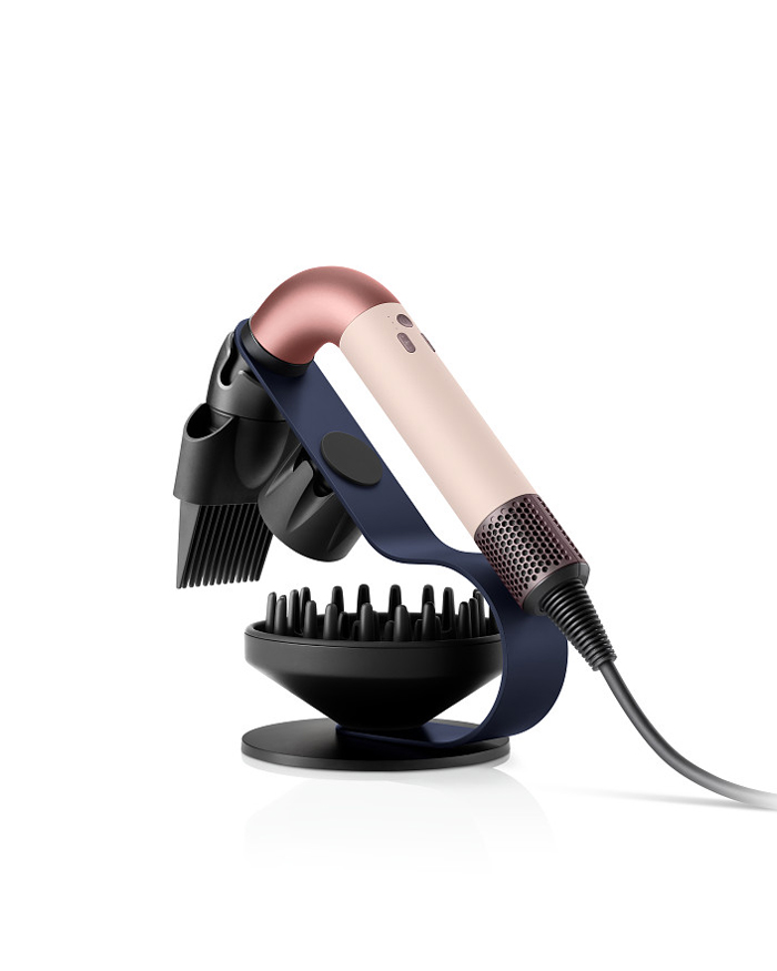 Dyson Supersonic R Haartrockner in der Farbe Ceramic Pink, elegant auf einem glatten Untergrund präsentiert. Das Gerät zeigt das ikonische runde Design mit schlankem Griff und hochwertigem Finish