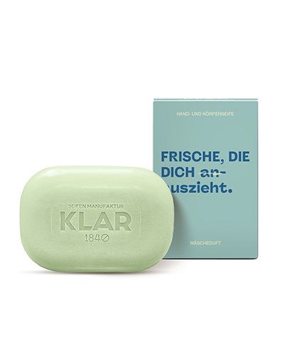 Hand- und Körperseife von Klar Seifen in zartem Grün mit Verpackung in Blau, Aufschrift 'Frische, die dich auszieht', nachhaltige Pflege mit angenehmem Wäscheduft – plastikfrei und vegan.